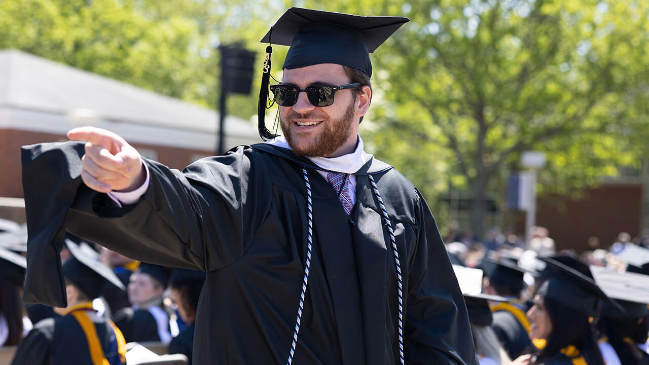 graduate smiles and points at something off camera