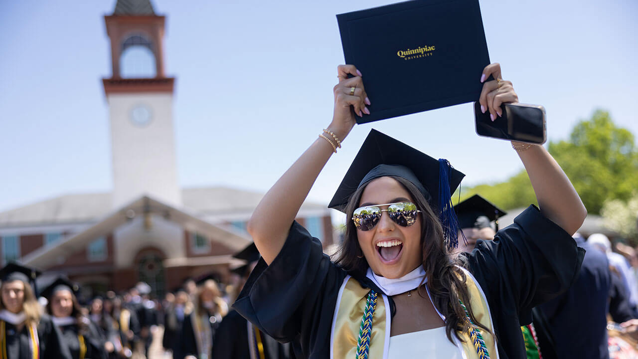 graduate raises her diploma above her head and cheers