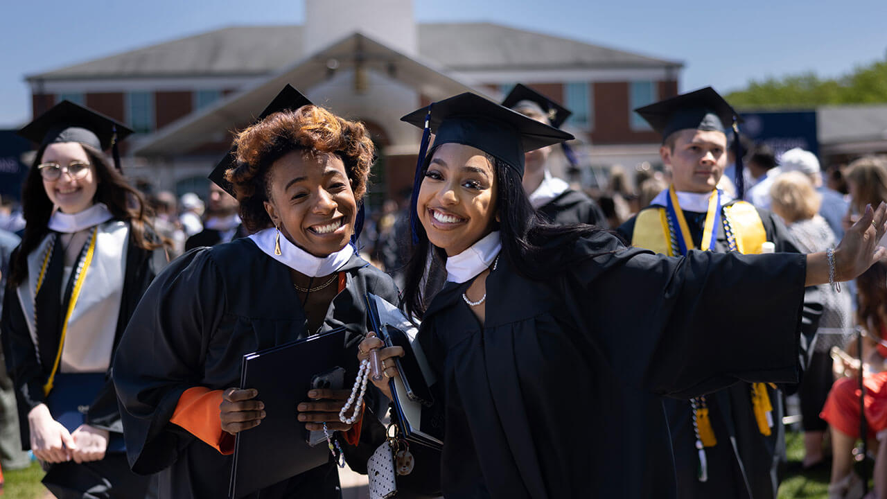 two graduates pose together and grin broadly