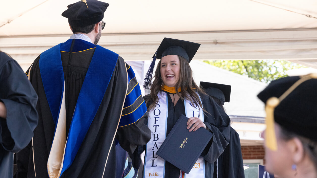 A graduate wearing a softball stole shakes hands with the dean