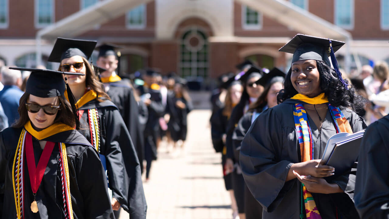 Graduates smile while holding diplomas in a line