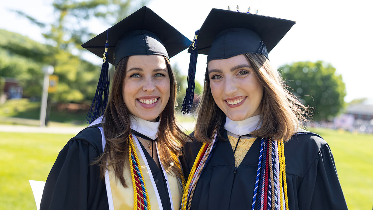 Two graduates from the School of Communications pose on the Quadrangle