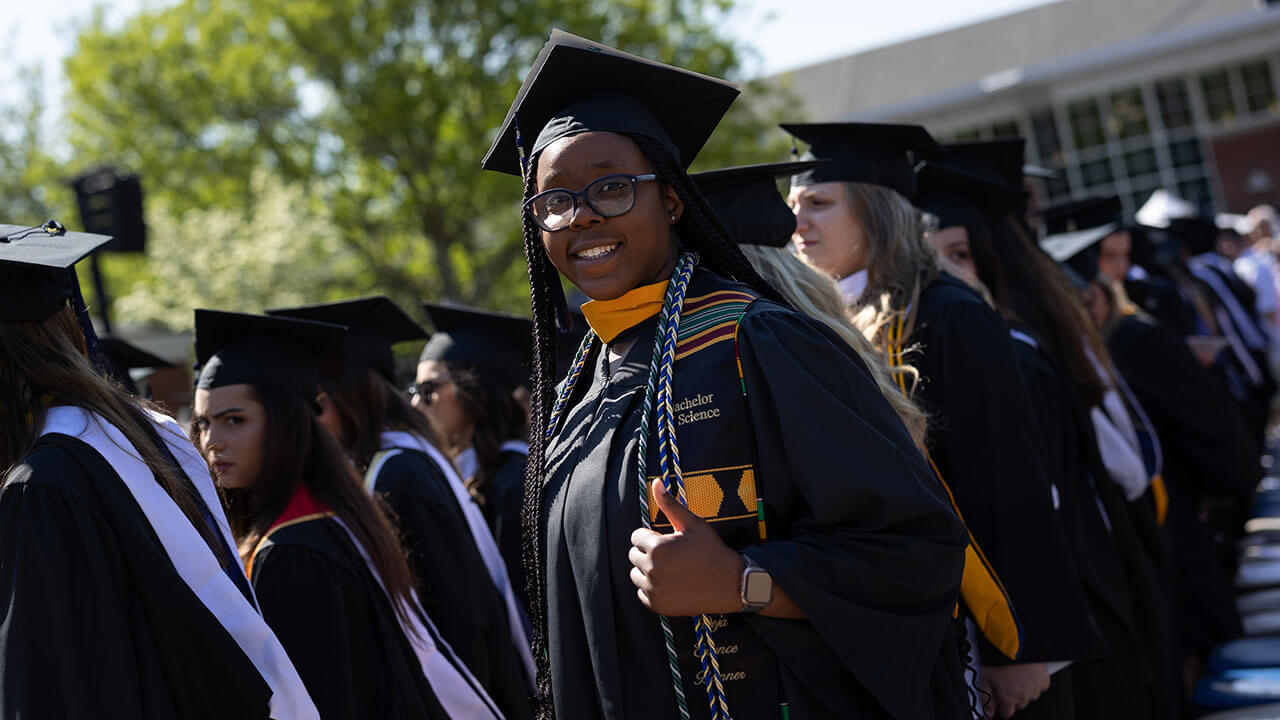 graduate gives the camera a thumbs up during the graduation ceremony