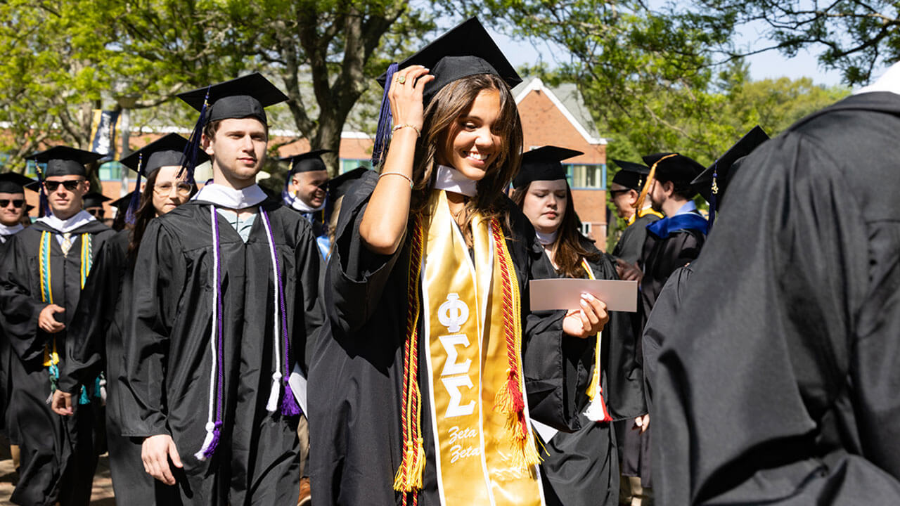 graduates walk down the center aisle, one holding her cap in the wind