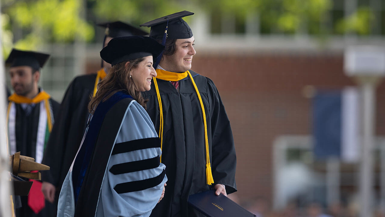 male graduate poses side by side and smiling with dean holly raider