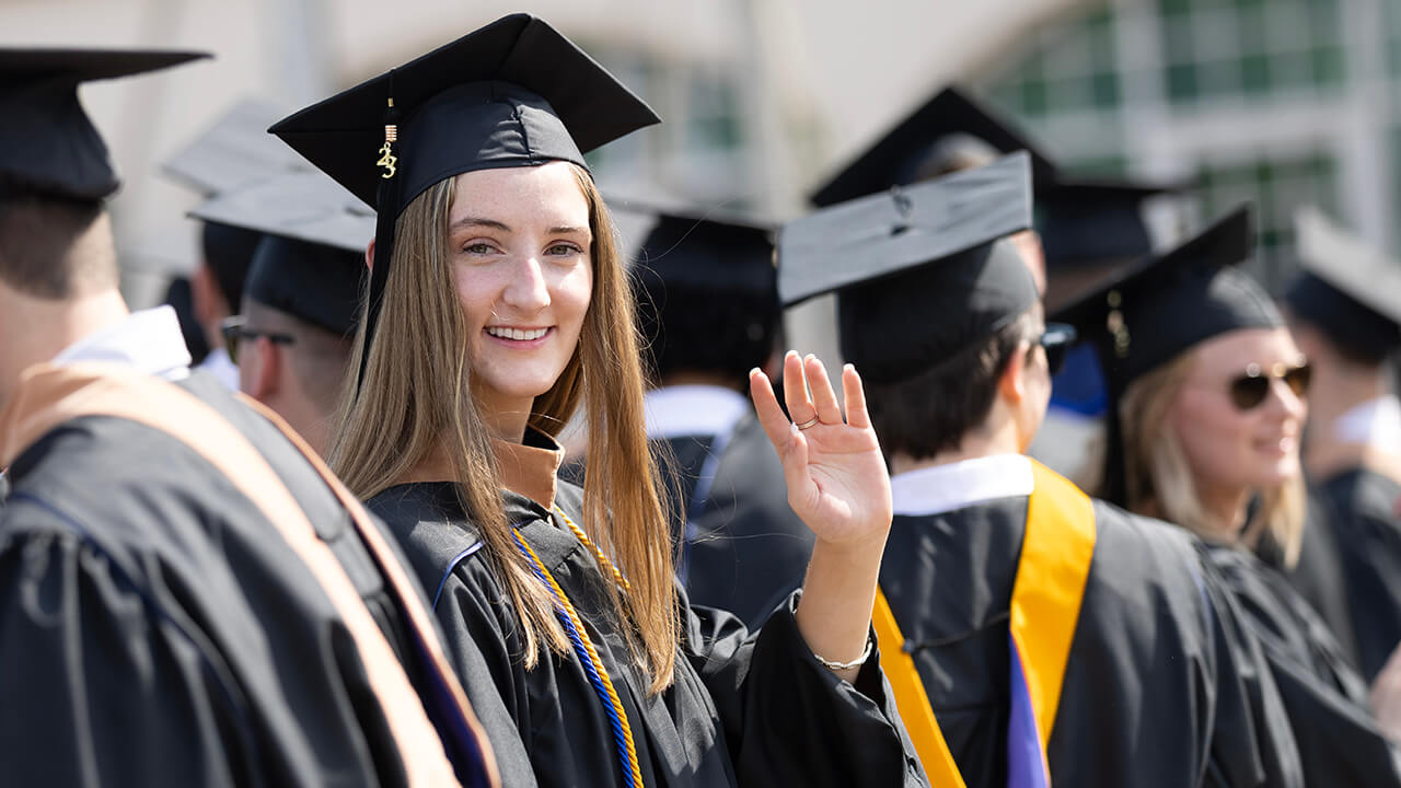 Graduate turns away from the line to wave towards the camera