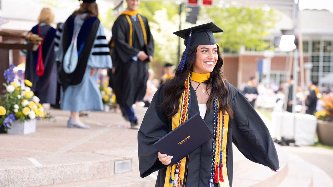 Student smiling ear to ear while holding her diploma and walking off stage