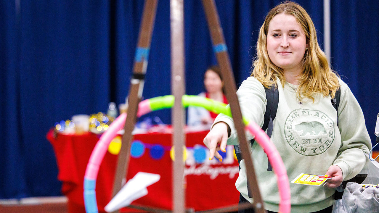 blonde haired female student throws a paper airplane through a colorful hoop