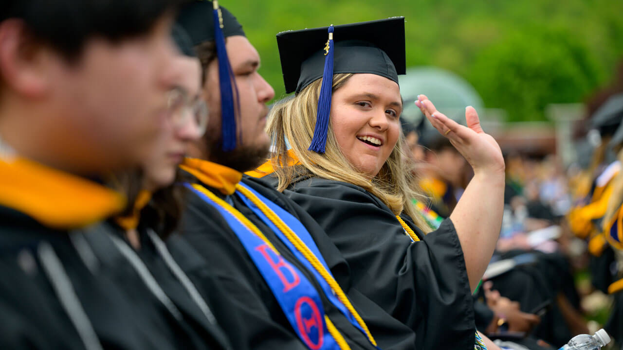 Graduate sitting and waving in the crowd while waving