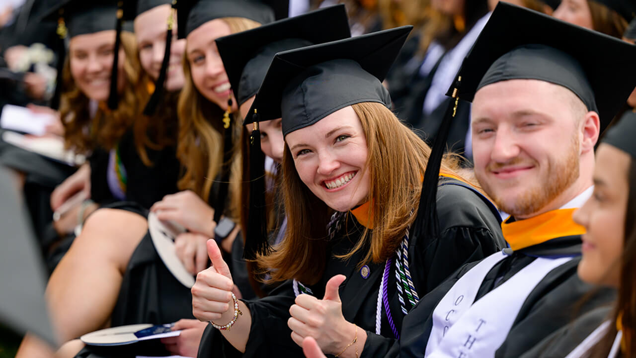 Graduate smiles for the camera while seated and gives a thumbs-up