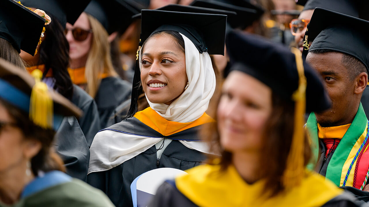 Graduate seated in the crowd looks toward the stage