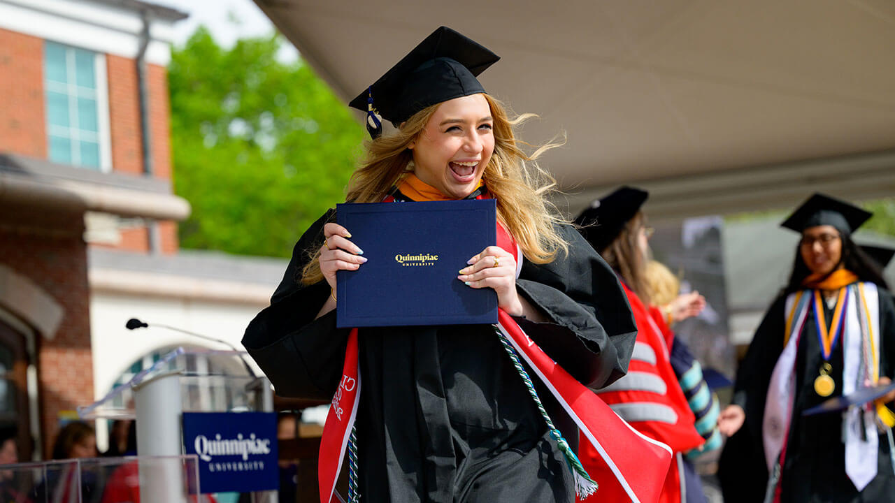 graduate holds up her diploma with a large grin on her face