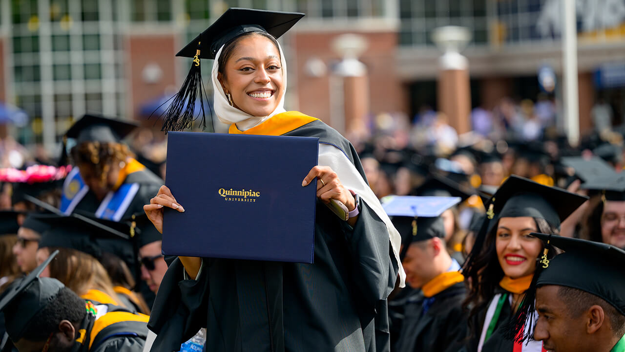 Student stands in the crowd and poses with diploma