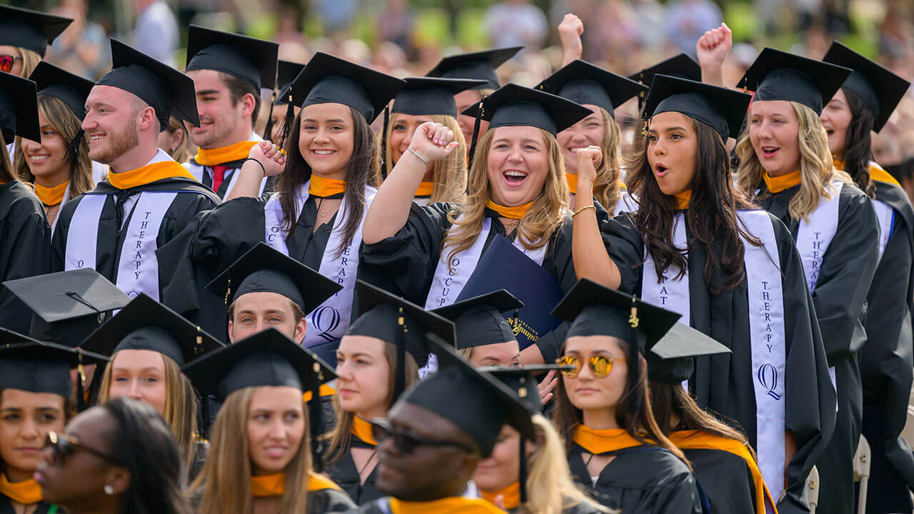 group of graduates fist pump the air in their caps in gowns from their seats