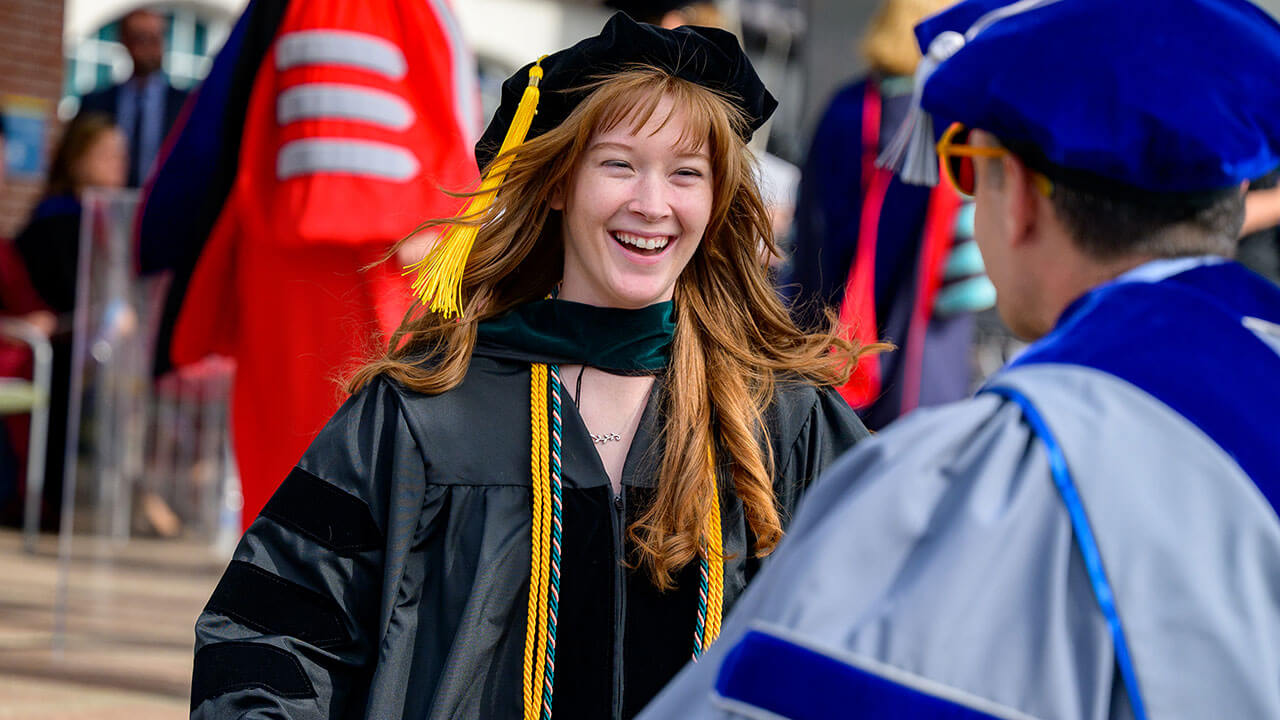 female graduate grins widely as she goes to hug a professor