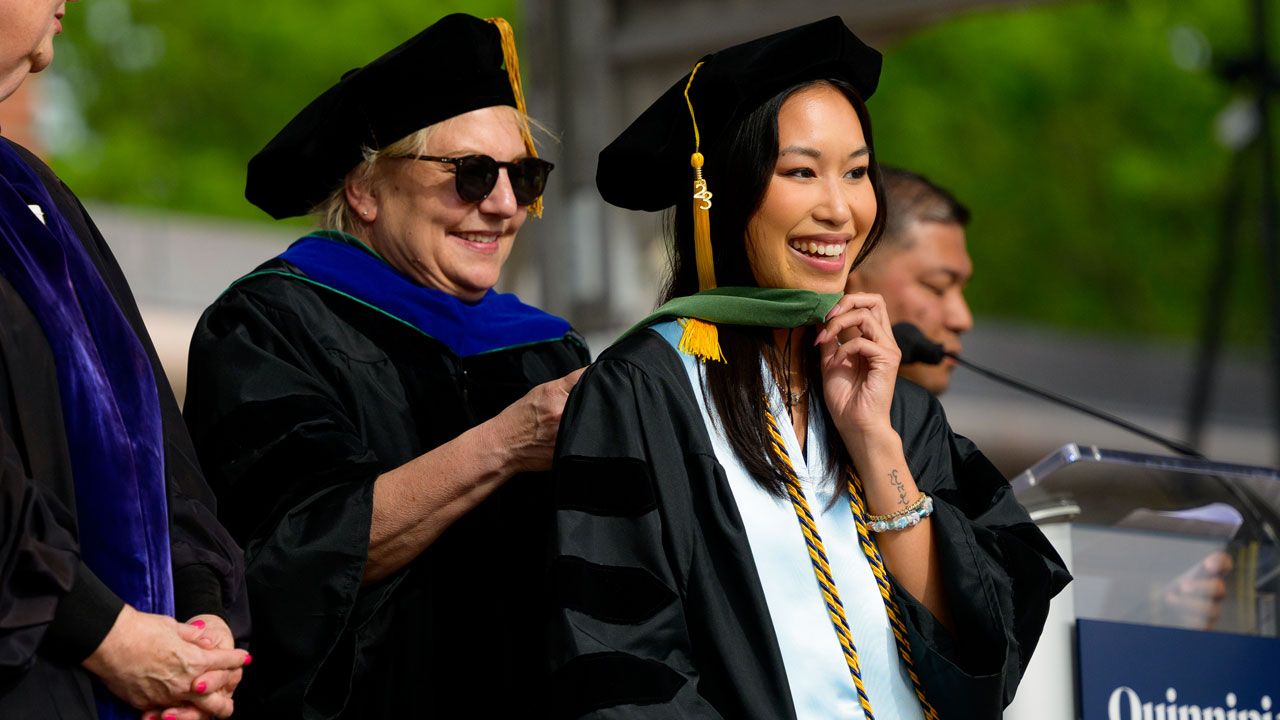 Graduate is hooded by her professors and all are smiling