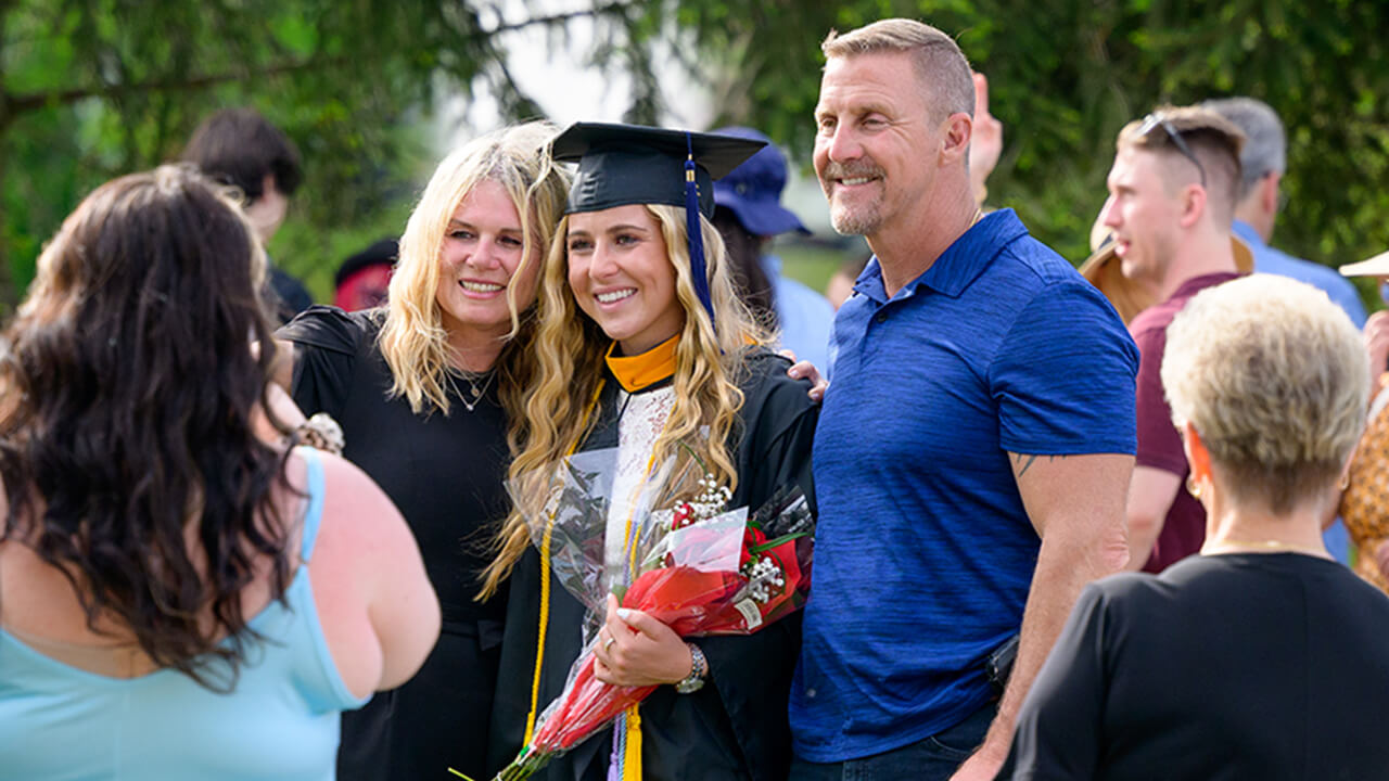 Family poses in front of pond fountain with their graduate and diploma