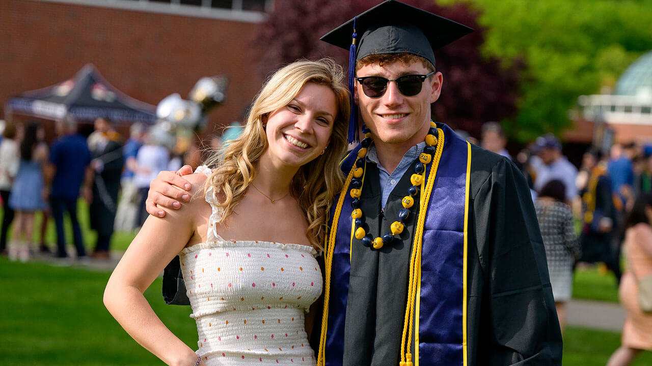 male graduate hugs a friend on the quad