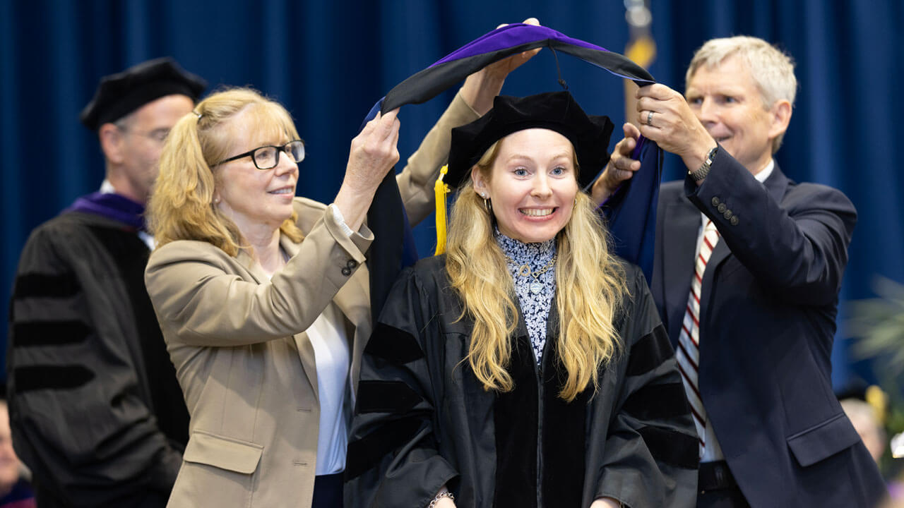 Student hooded smiling ear to ear with excitement on stage