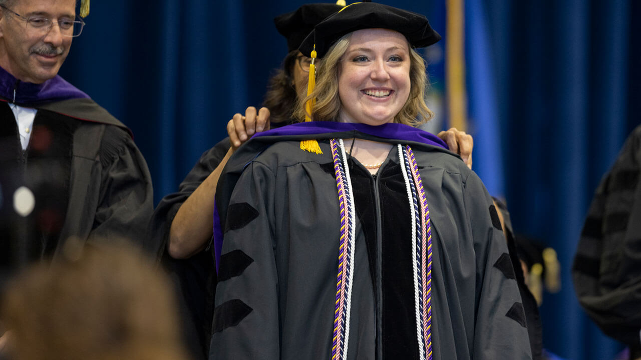 Student rewarded hood with her professors smiling