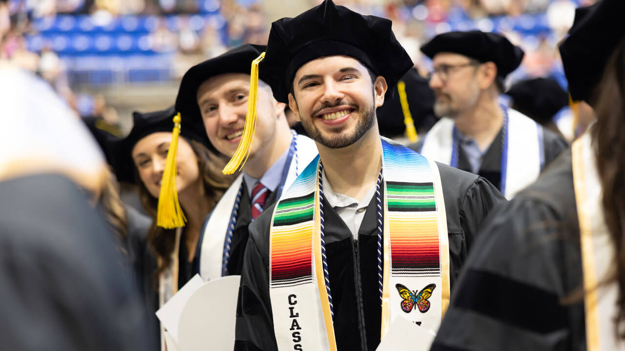 Students formed in line smiling and prepared to receive diploma