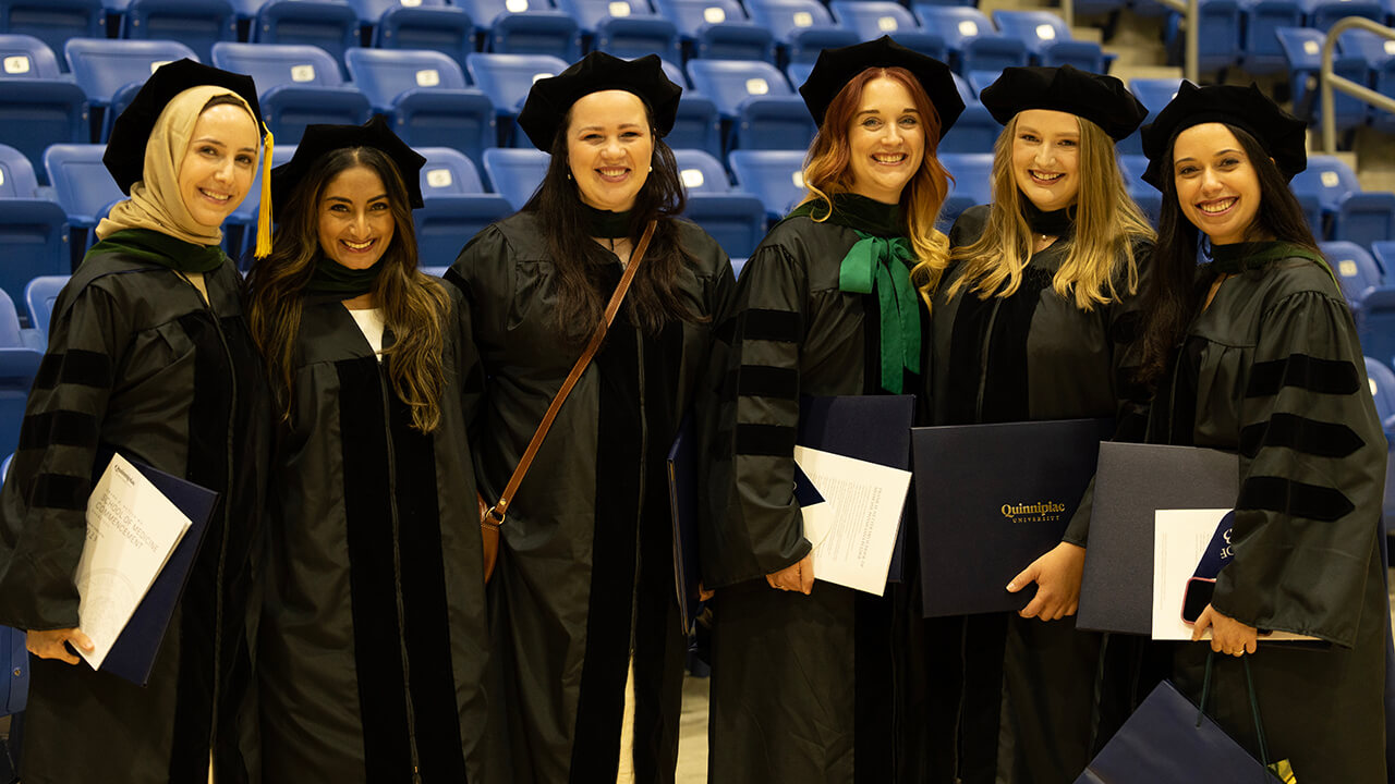 Graduates gather and smile for a photo in front of the stands