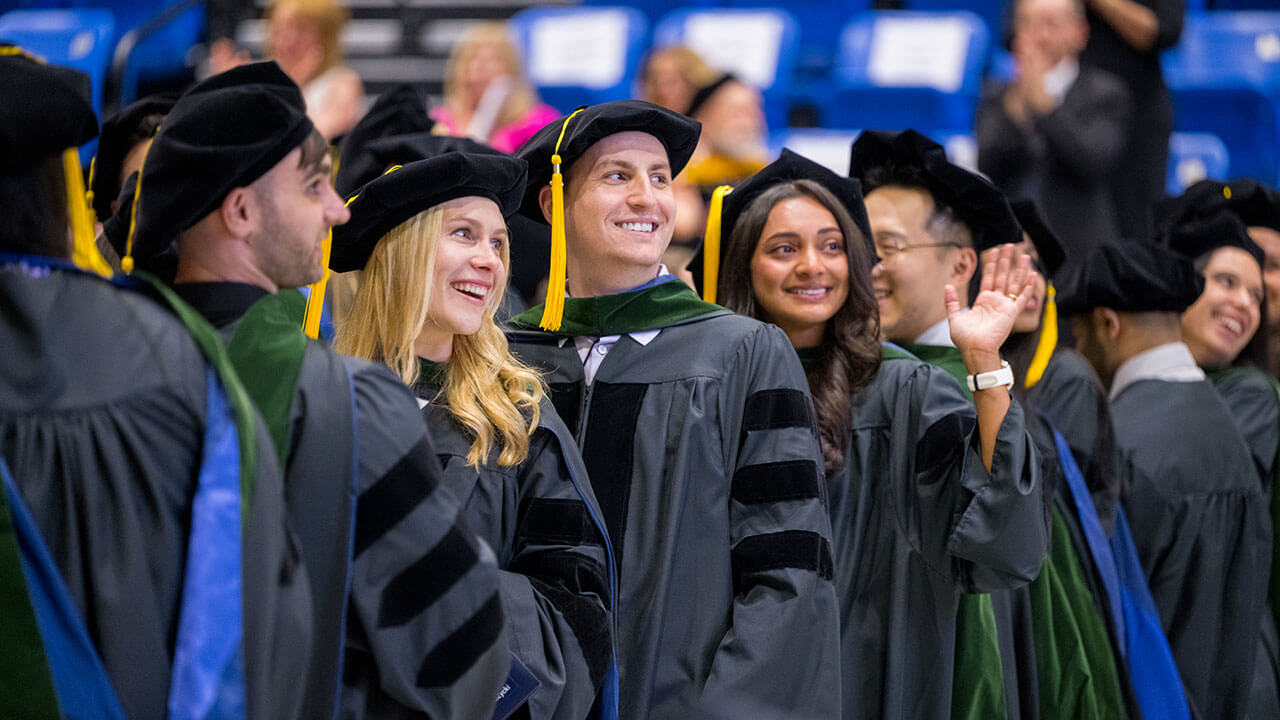 graduates turn to smile and wave at their audience