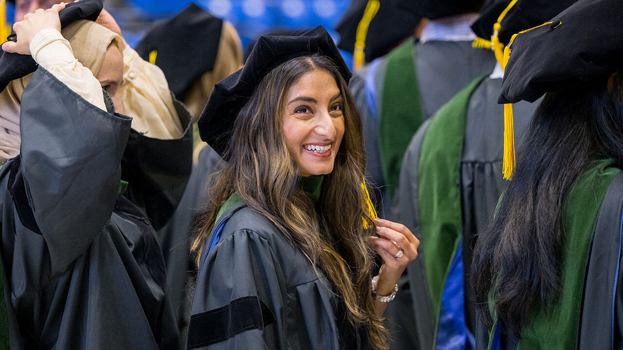 graduate with long brown hair smiles and holds her tassle