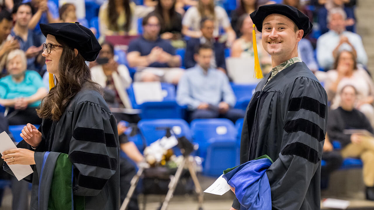 Graduates stand in line and one smiles for camera