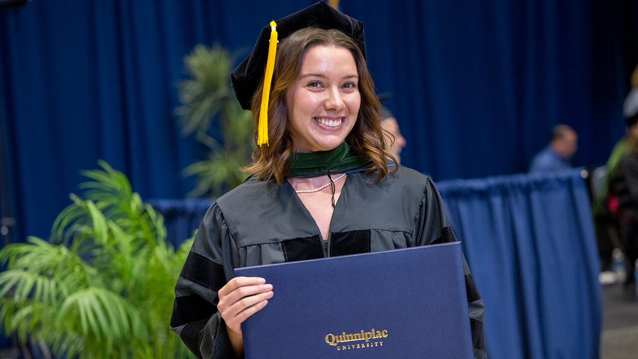 Smiling graduate poses after receiving diploma on stage