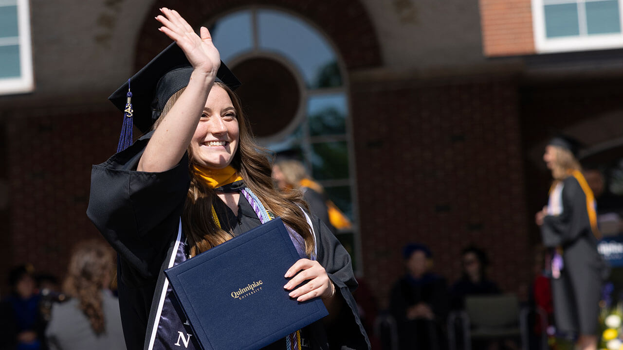 graduate grins broadly while waving to the audience