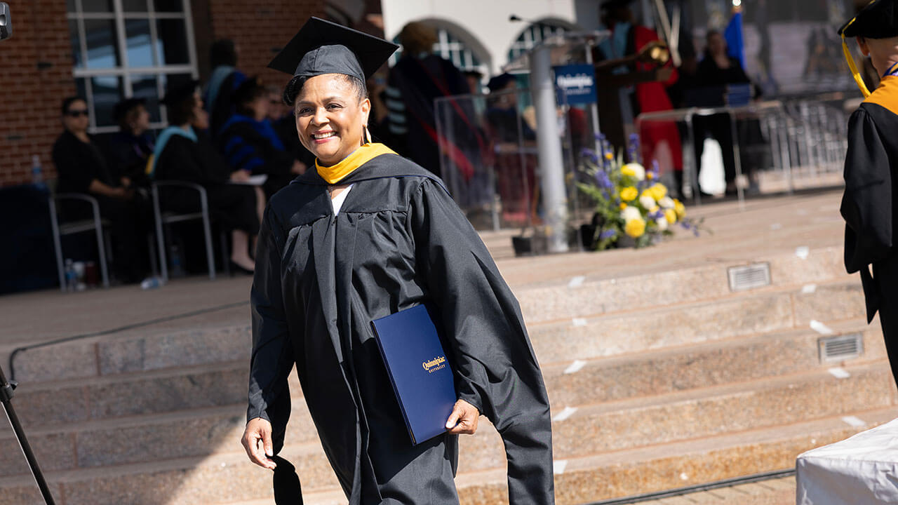 A graduate holds her diploma and walks across the library steps