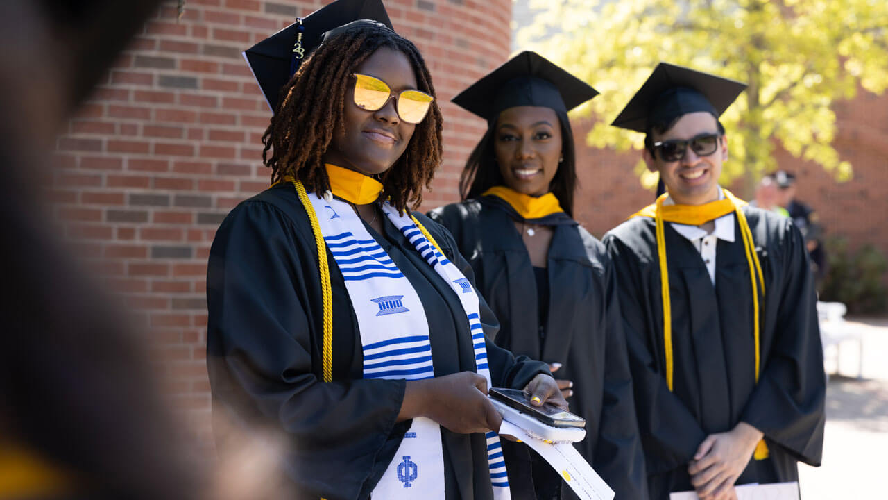 Three graduates grinning and standing in line