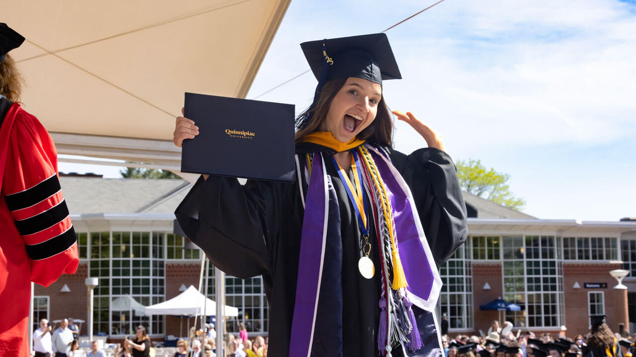 Graduate sways her arms in the air holding her diploma and smiling