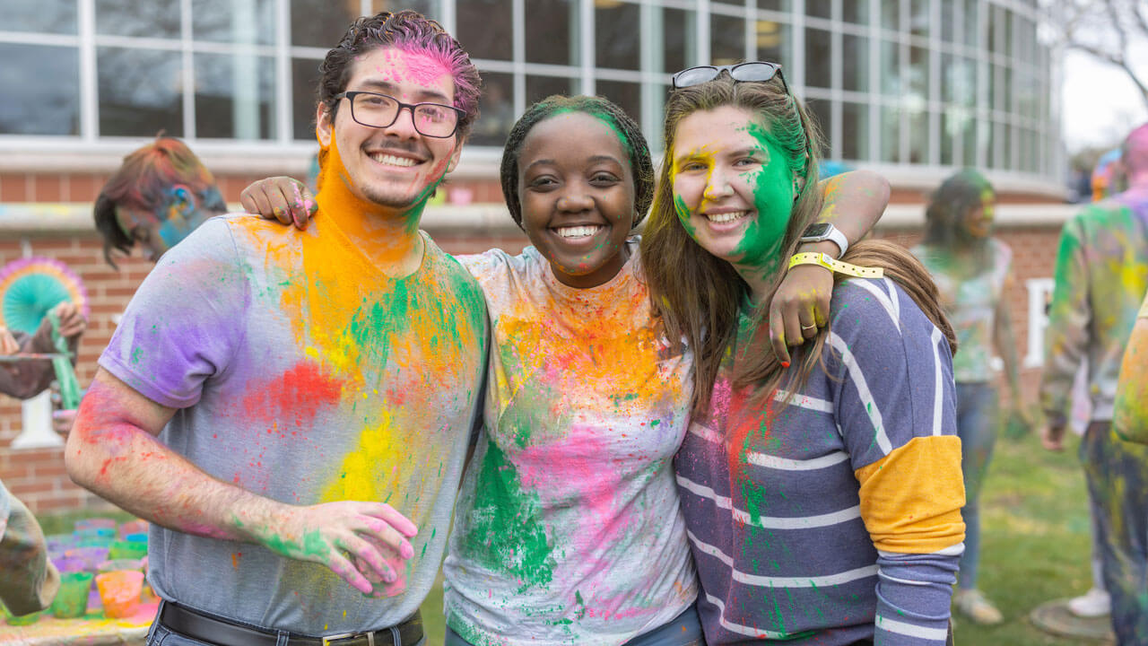 Three students smile together at Holi celebration