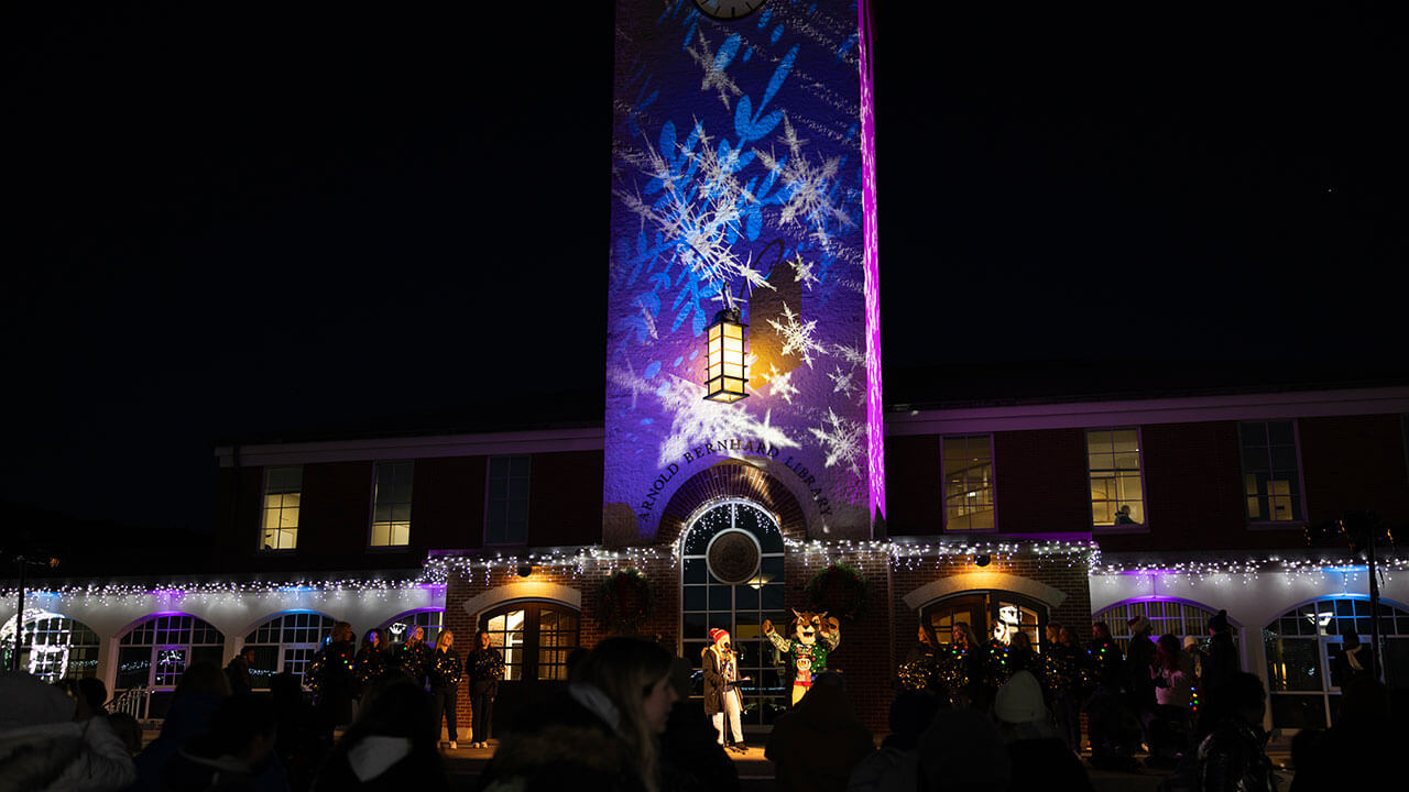 Intricate blue and purple lights shine onto the Arnold Bernhard Library with a crowd looking up at it