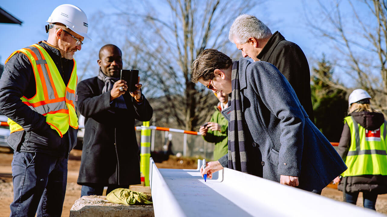 QU staff crowd around a beam for the South Quad and sign it.