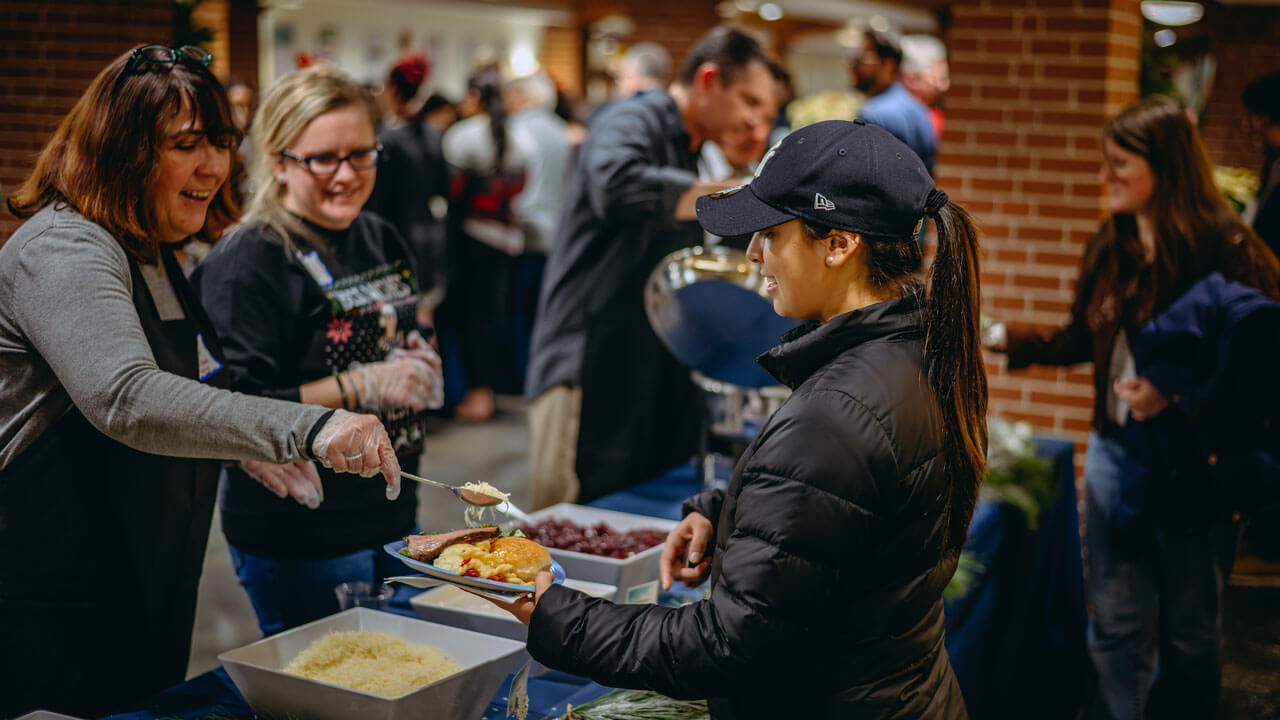 Smiling professors serving food at their station to students