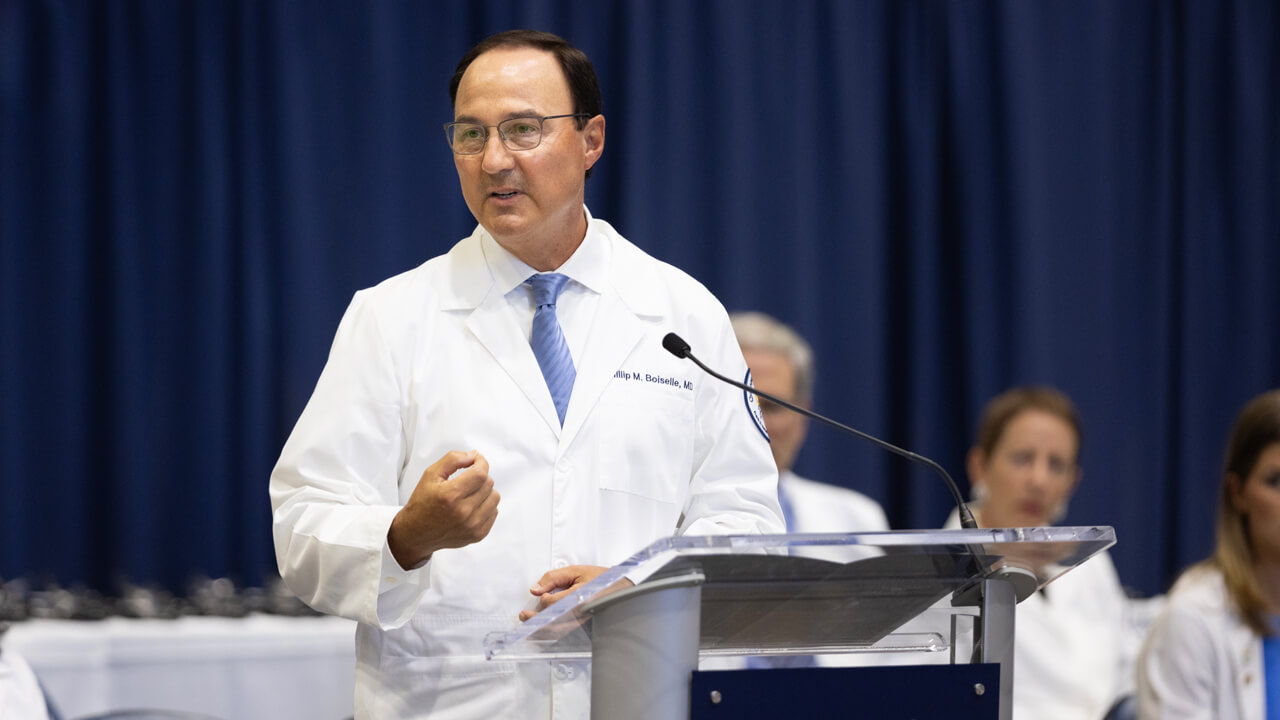 Dean Boiselle wears his white coat and speaks from a podium