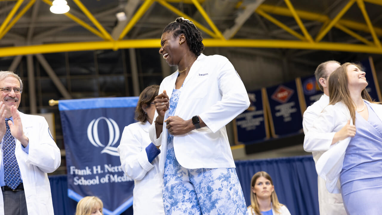 A student pulls her coat close and smiles at faculty on the stage