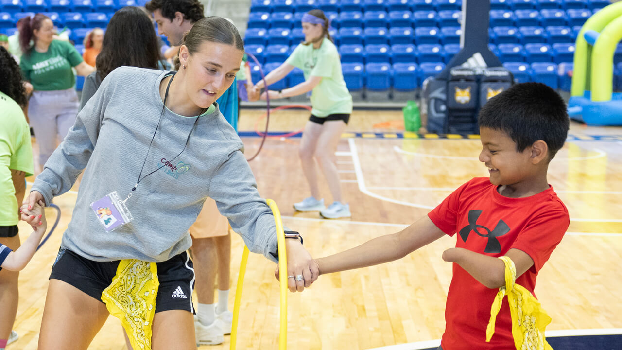 Two individuals hold hands with a hula hoop