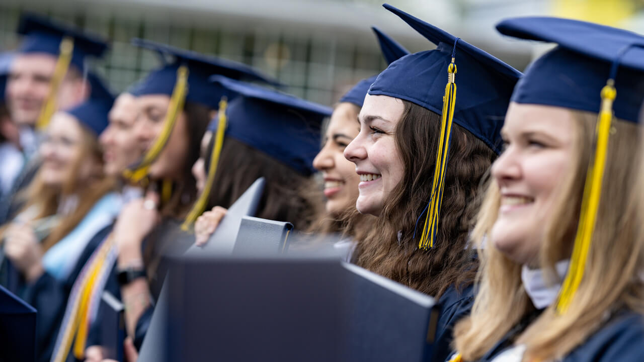 A row of graduates hold up their diplomas and smile