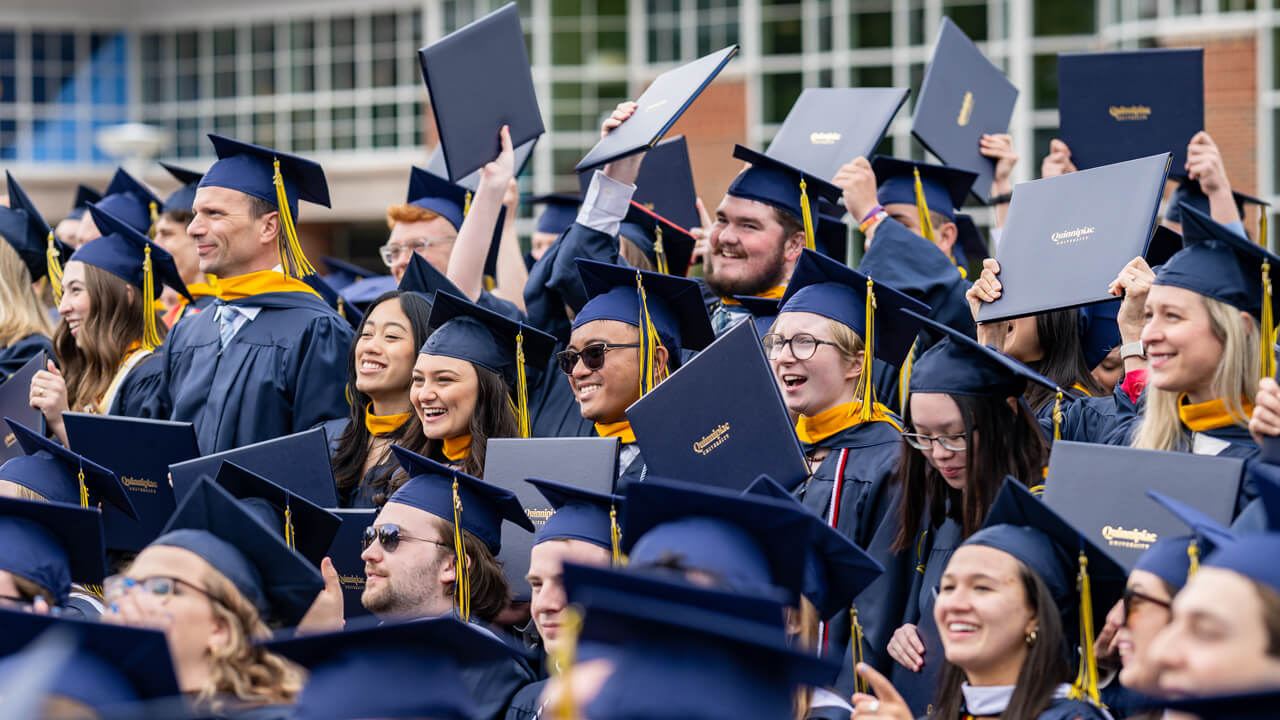 Hundreds of graduates cheer, smile and hold up their diplomas