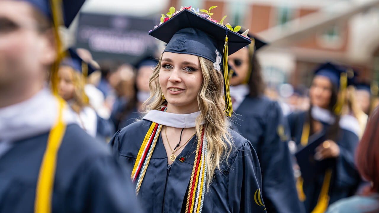 A graduate with dozens of colorful flowers on her cap walks in front of the library