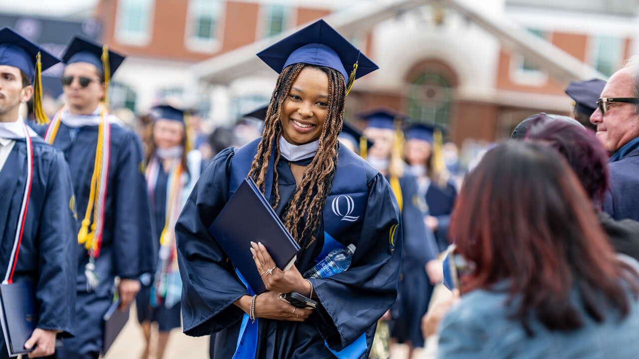 A graduate holds her diploma and pauses for a photo for her family member