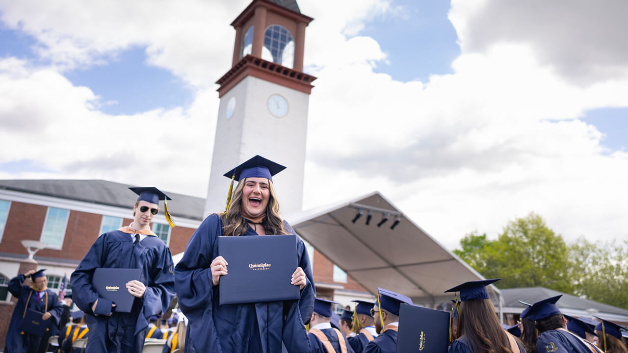 Student holds degree in front of clock tower