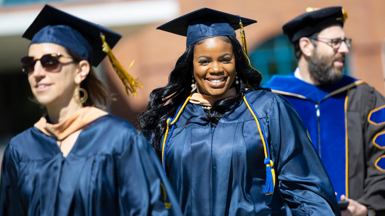 Brown hooded MBA graduate beams in their cap and gown.