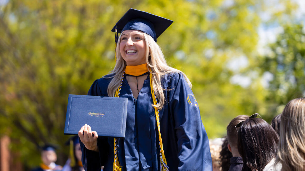 Student smiles holding diploma after crossing the commencement stage