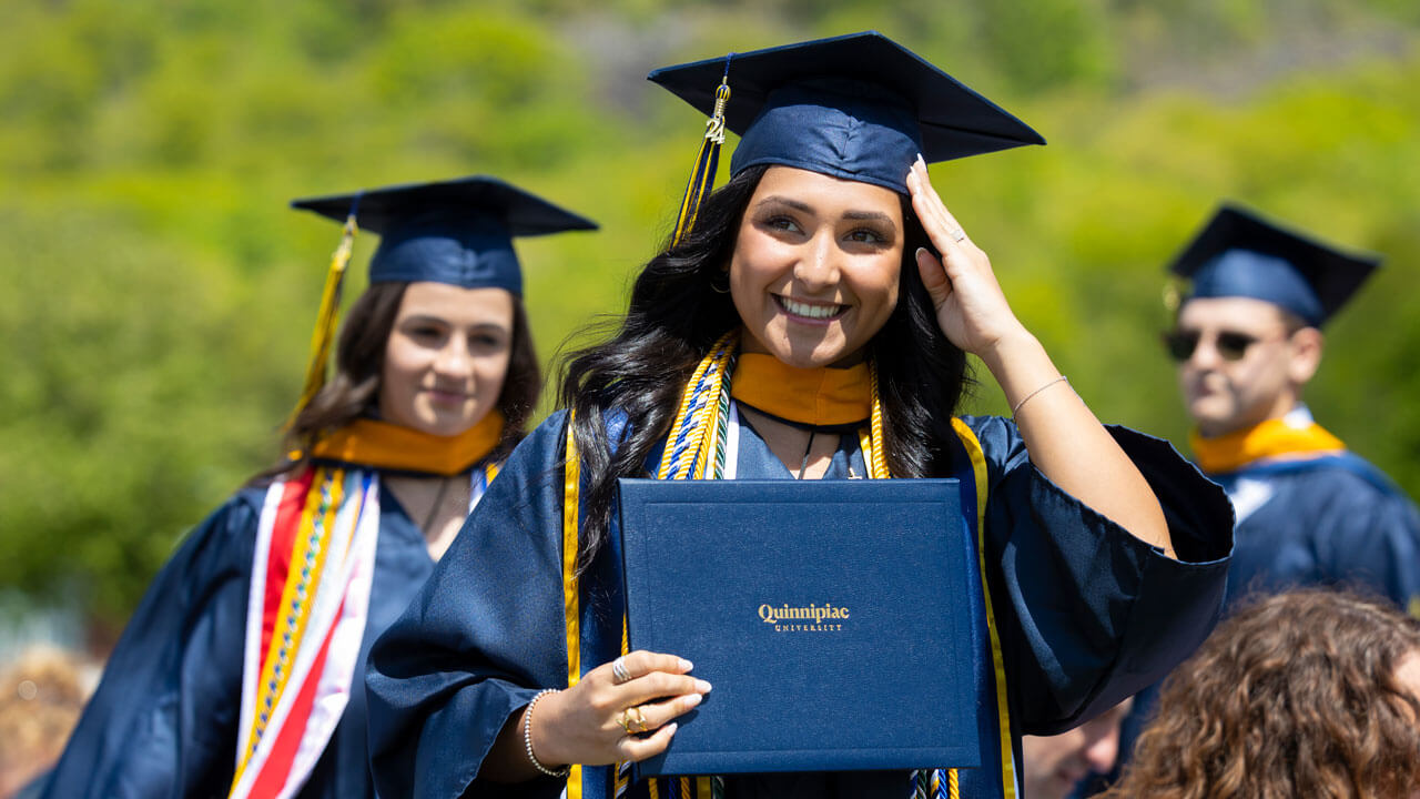 Student in gap and gown smiles whole holding diploma