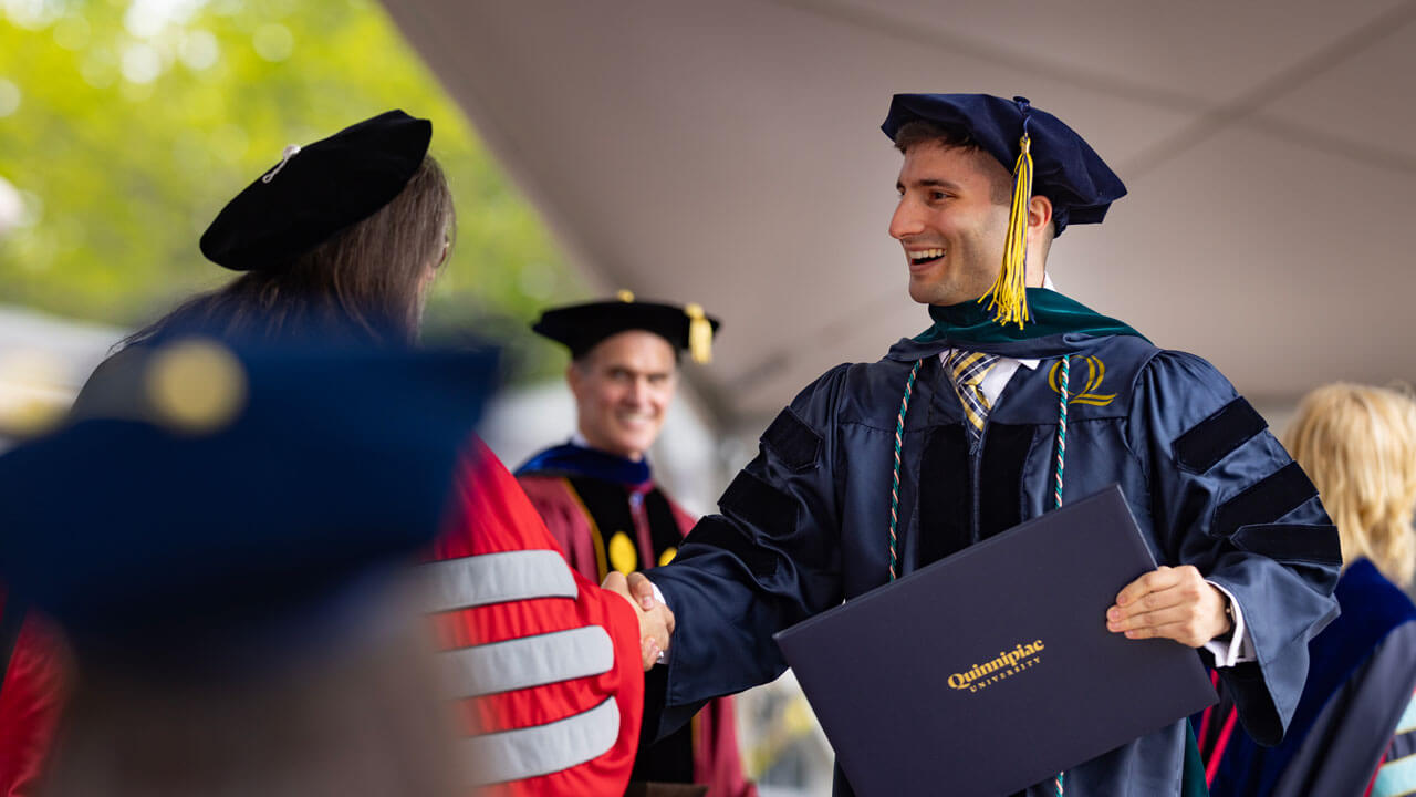 A graduate from the Health Sciences class of 2024 delivers a handshake after receiving their diploma.